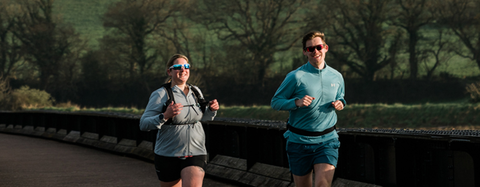 A woman and a man, running in rural areas, wearig shorts and sunglasses.