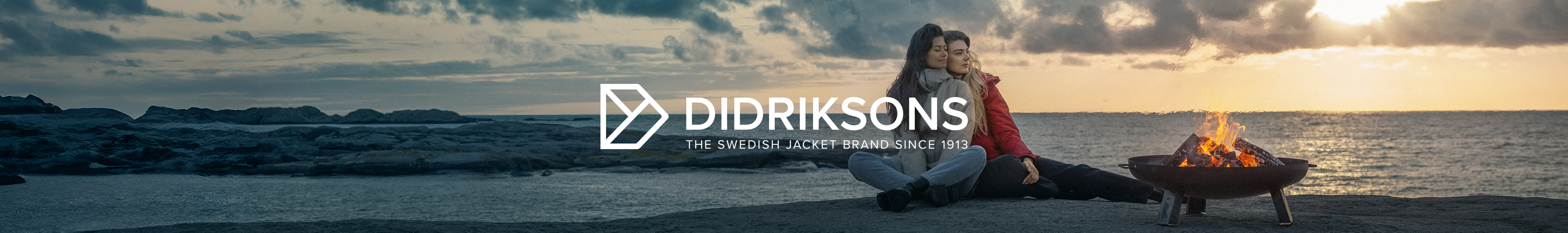 Two people are standing on a rock above the sea, wearing Didriksons jackets.