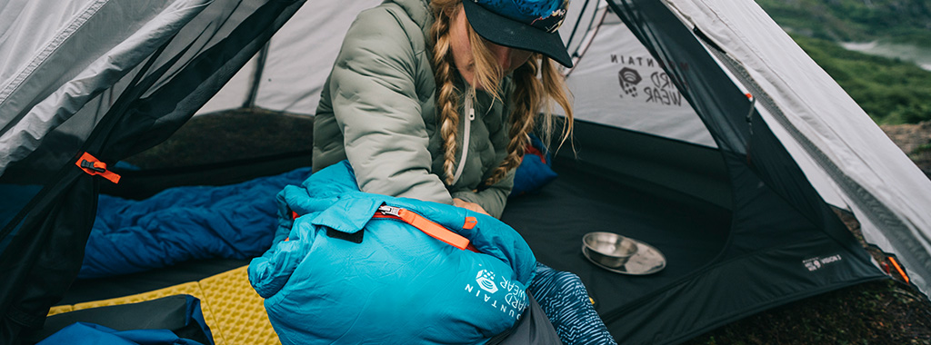 A woman sitting in the Mountain Hardwear tent and packing away her Mountain Hardwear blue and orange sleeping bag