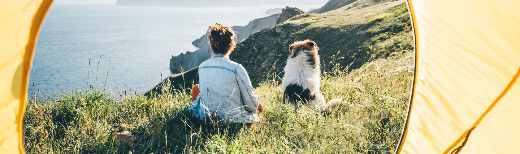 Dog and woman sat on the grass outside a bright yellow tent