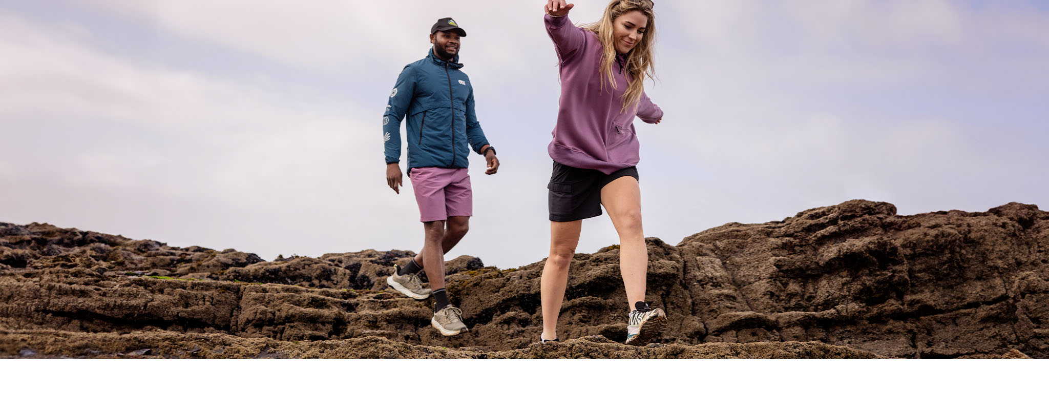 A man in pink shorts and a woman in black shorts walking towards the camera on a rocky outcrop