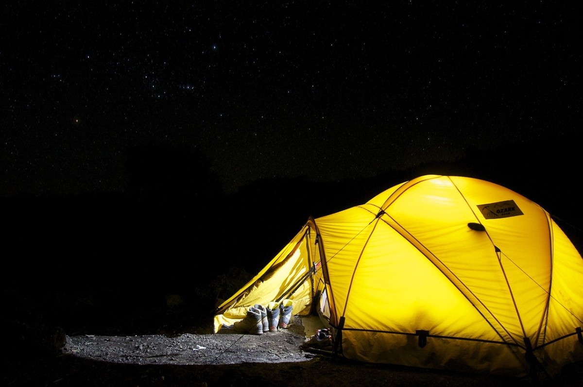 A tent pitched in the wild, glowing from the inside lamp in the darkness