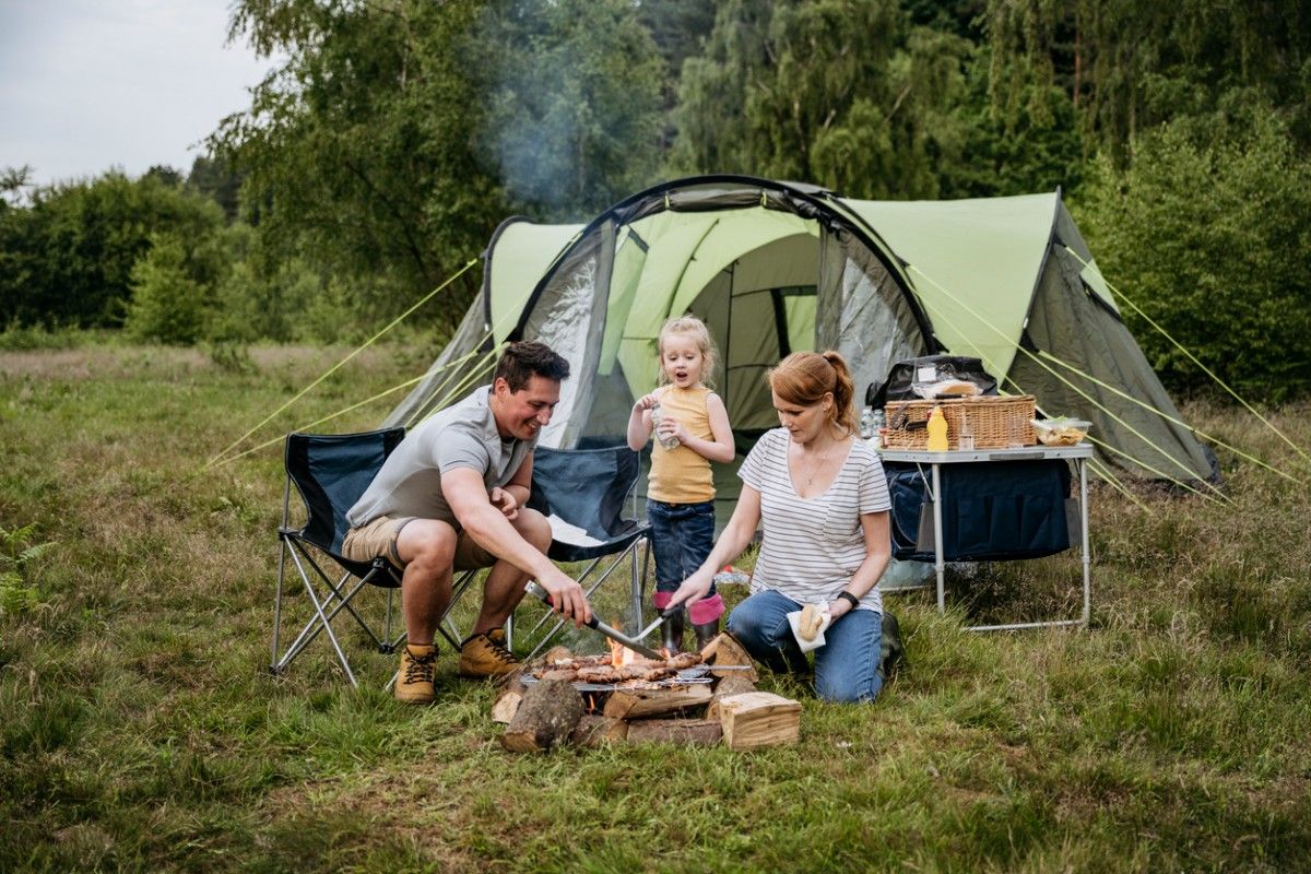 A family camping in Great Langdale, cooking over a campfire with their child 