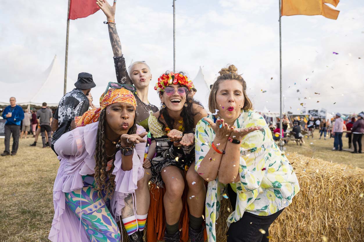 People blowing confetti at the camera at the festival in front of hay bayles 