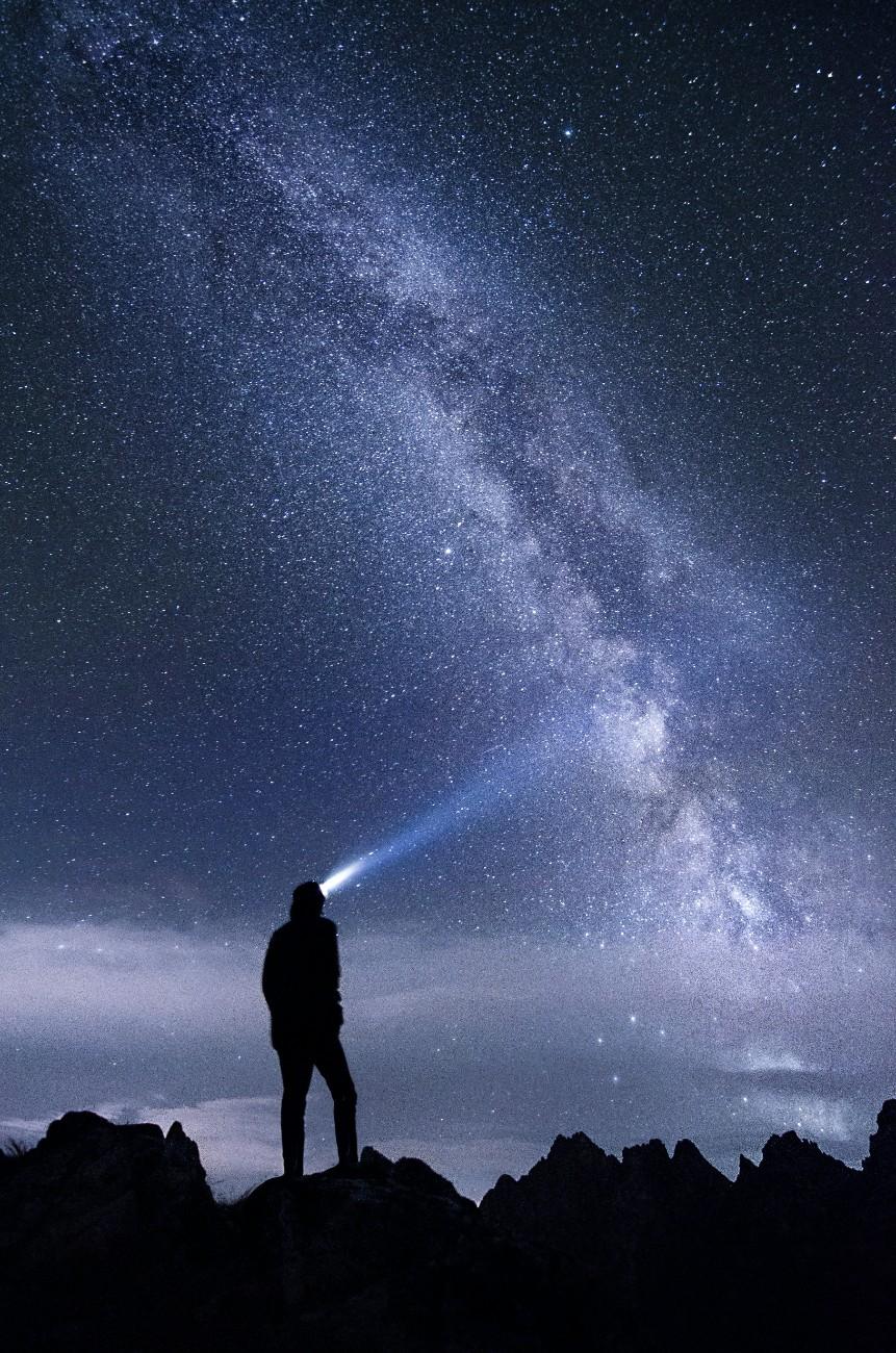 A man with a head torch on a night hike looking up at the starry sky 