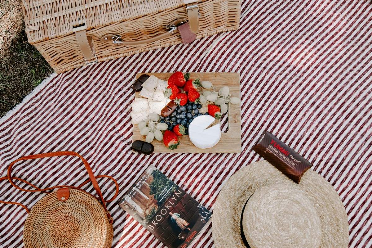 A picnic blanket with a basket and charcuterie board in the middle 