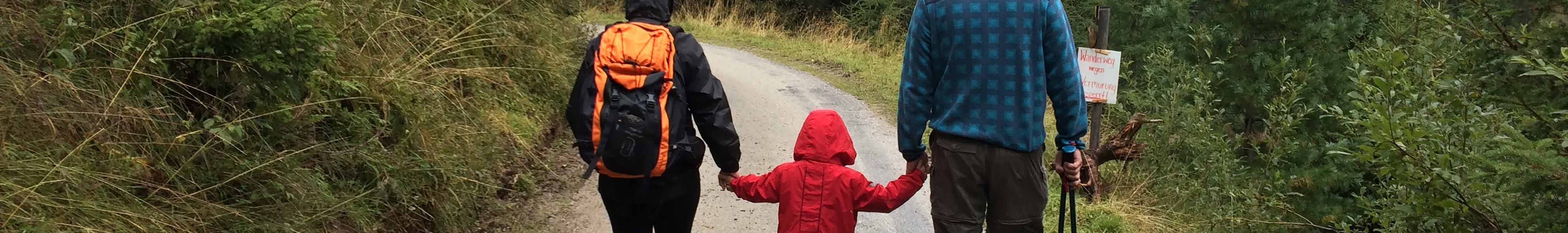 A child wearing a waterproof jacket, holding their parents' hands 