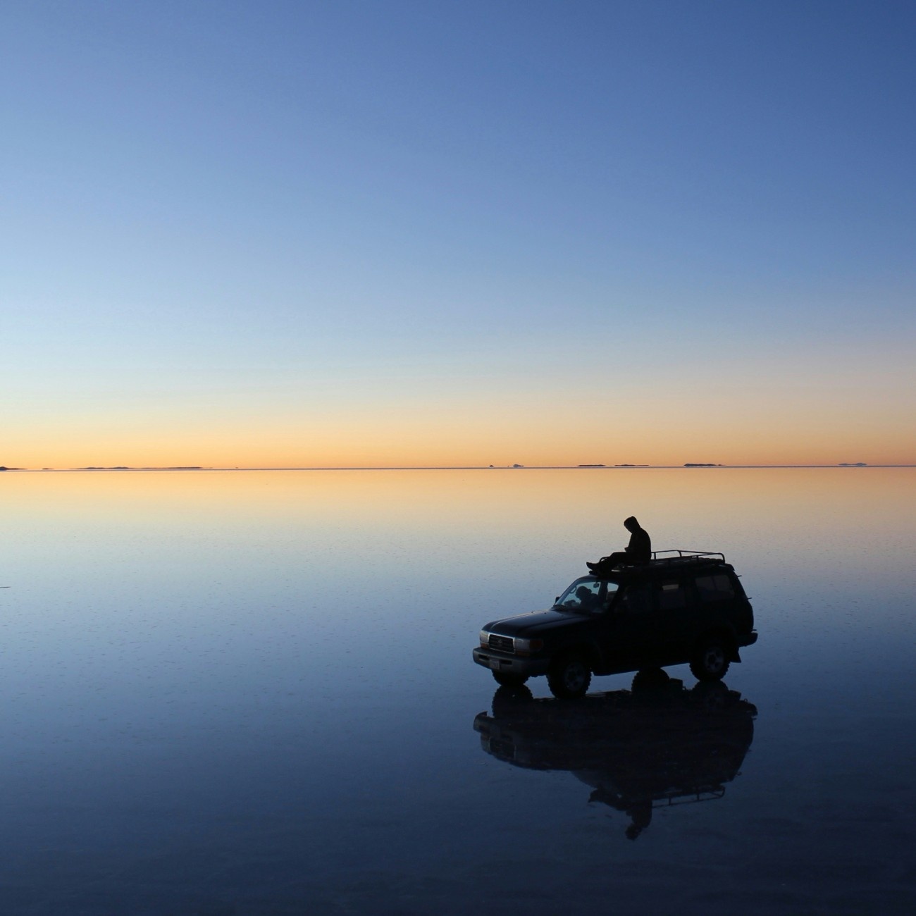 A person sat on the roof of a truck on the Salar de Uyuni salt flats at sunset 