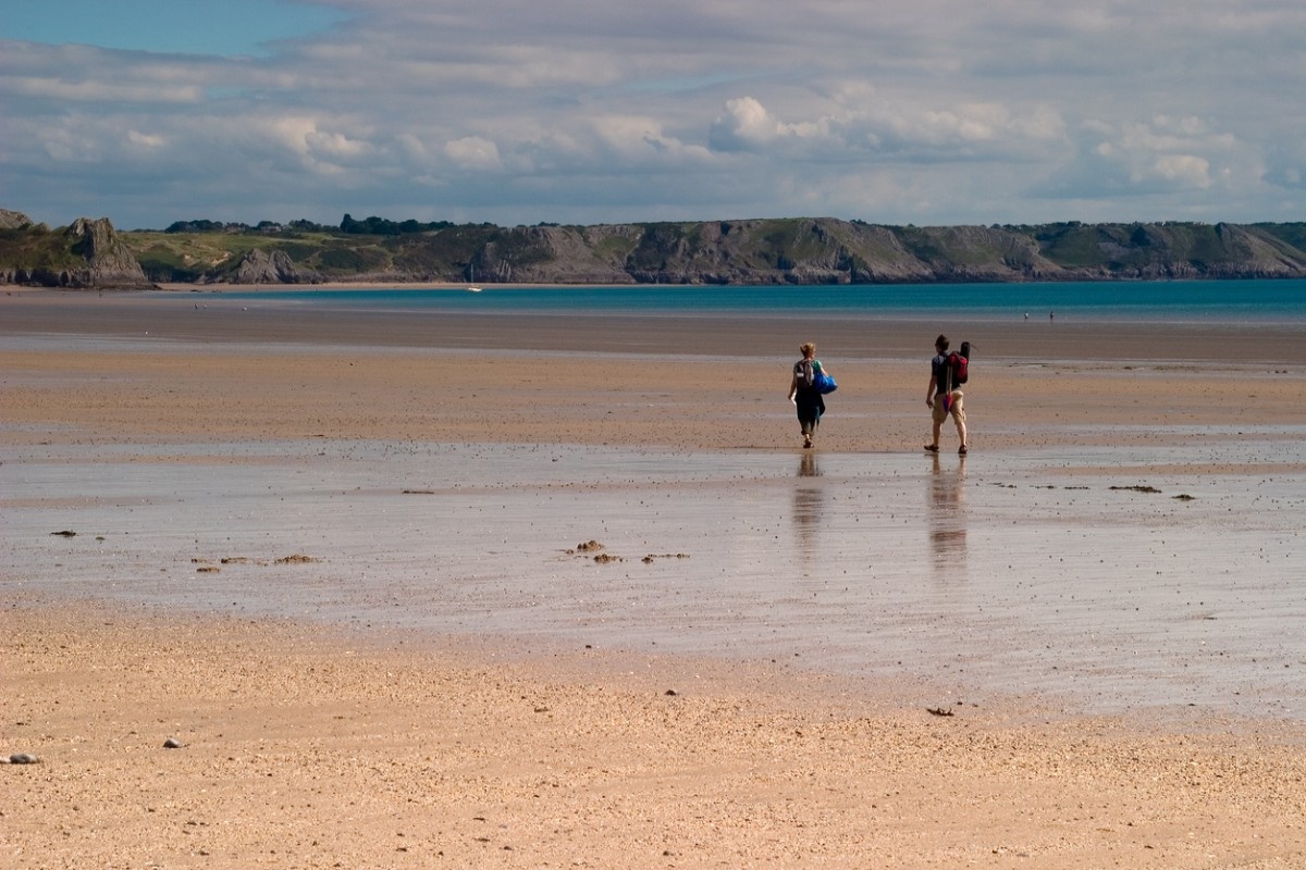 People walking along Oxwich bay beach