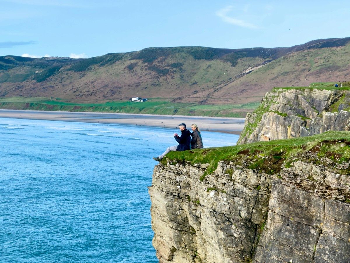 A couple sat on a cliff edge on Rhossili Bay