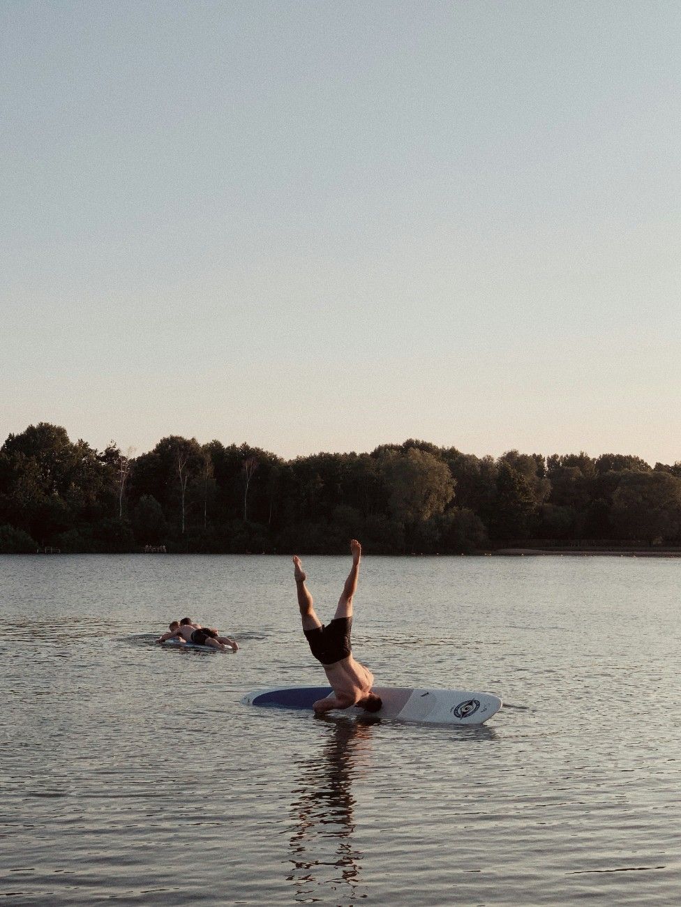 A man doing a headstand on a paddleboard, falling off