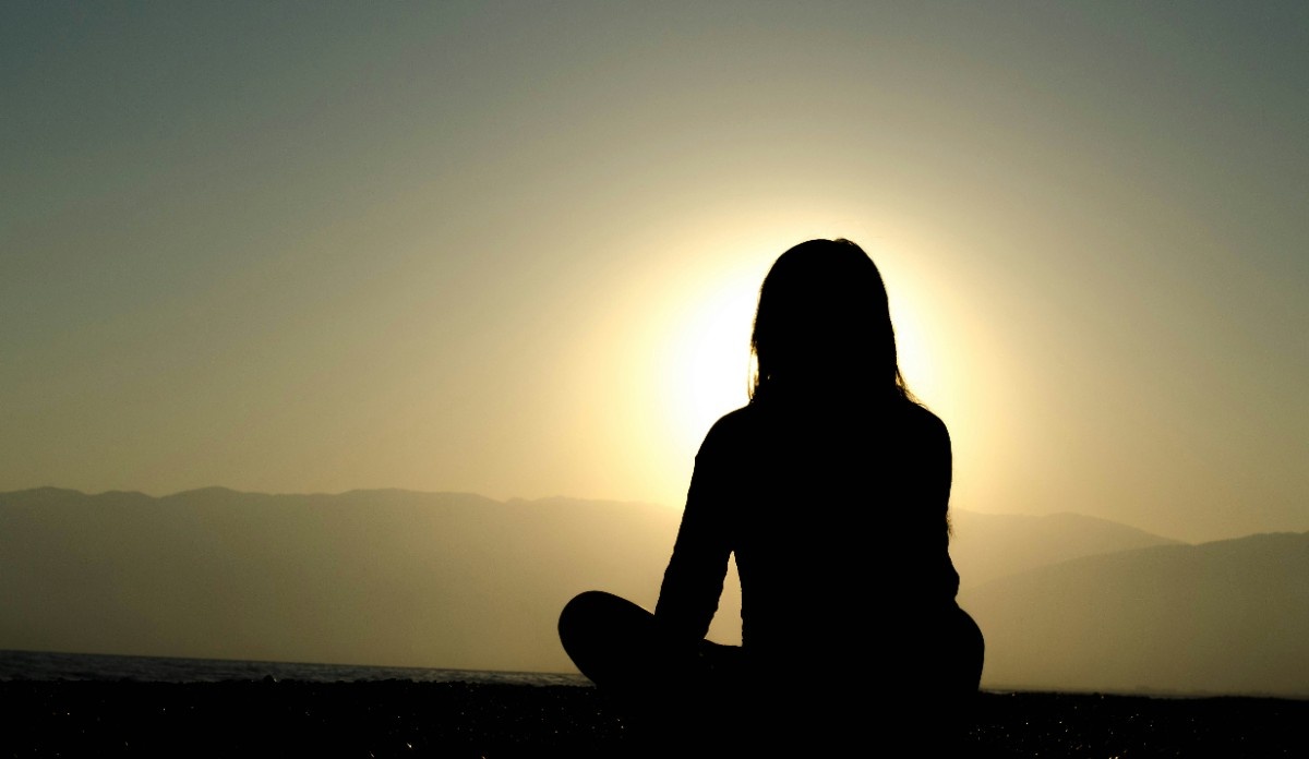 A person sat meditating outside as the sun sets 