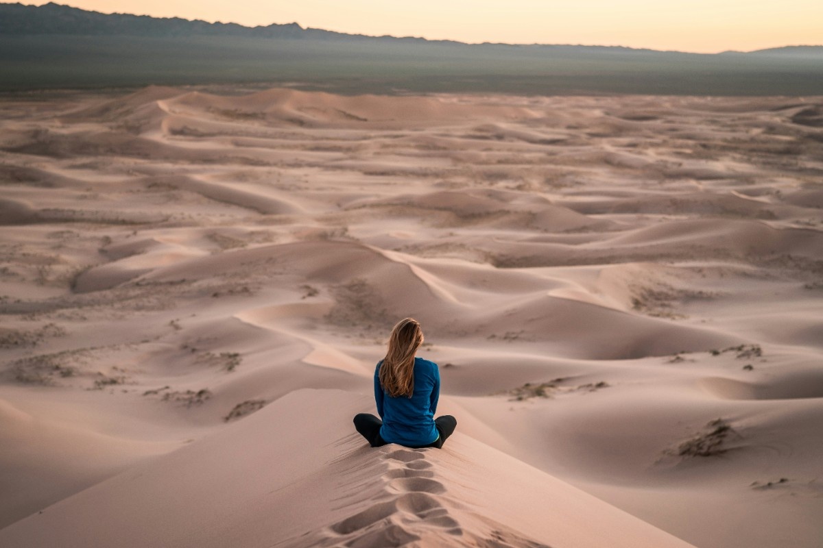 A person meditating on a sandy dune 