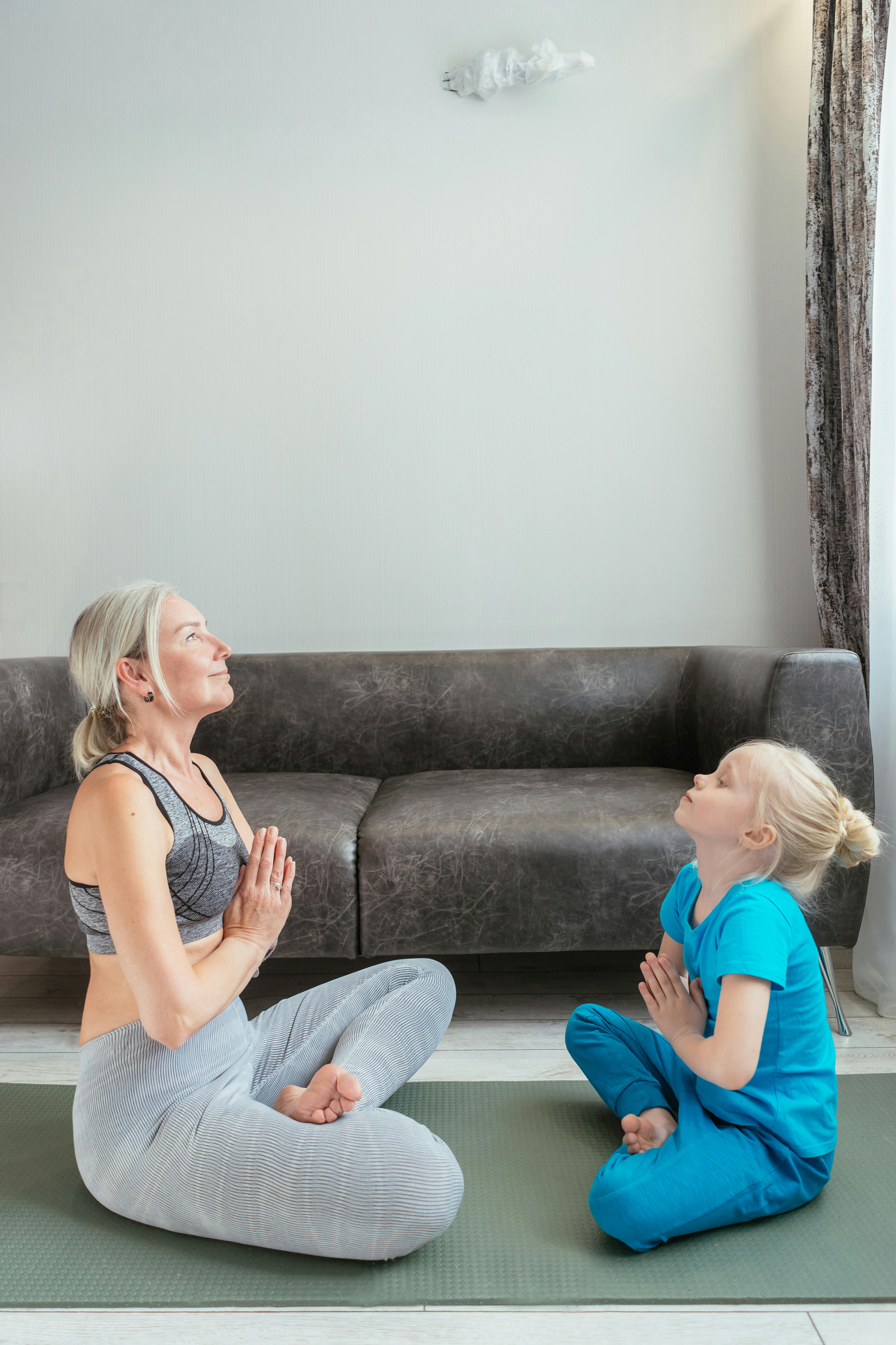 A woman and her daughter sat with their hands to heart centre, ready to do a yoga practice