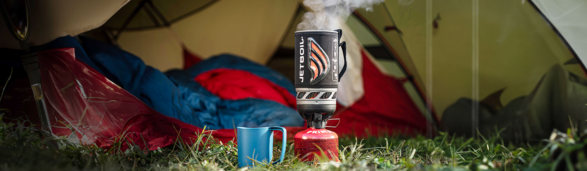 A blue cap and a Jetboil coocking system on grass next to a tent